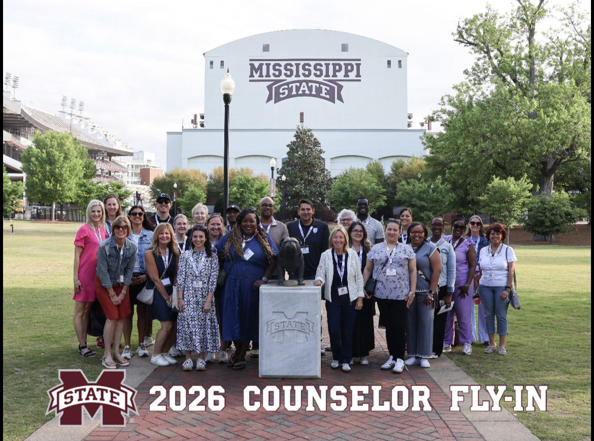 Group of people standing outdoors in front of Mississippi State building, some holding certificates, with trees and grass around.