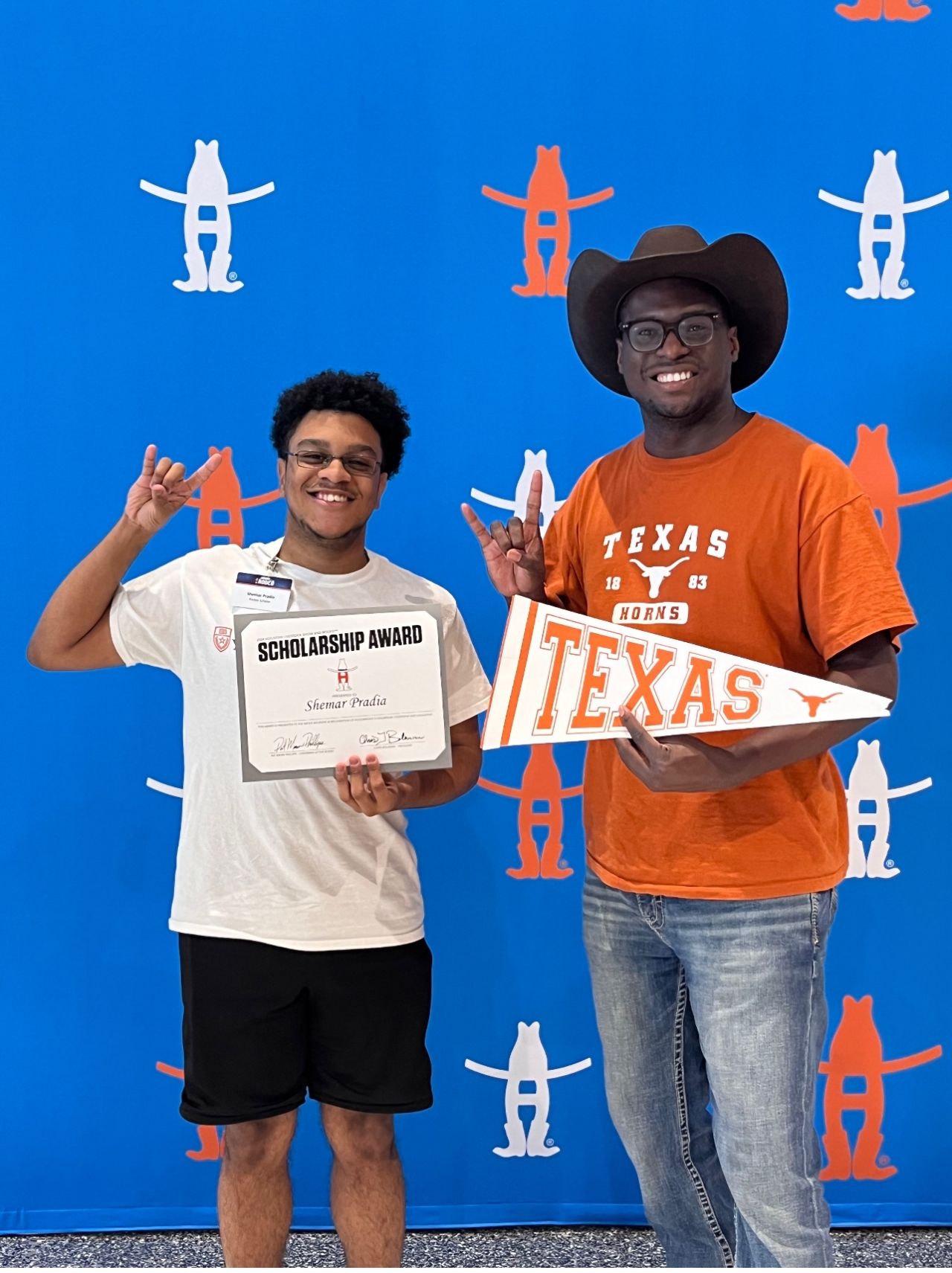 Two people smiling, one holding a scholarship award, the other holding a Texas sign, standing in front of a blue backdrop with Texas-themed figures.