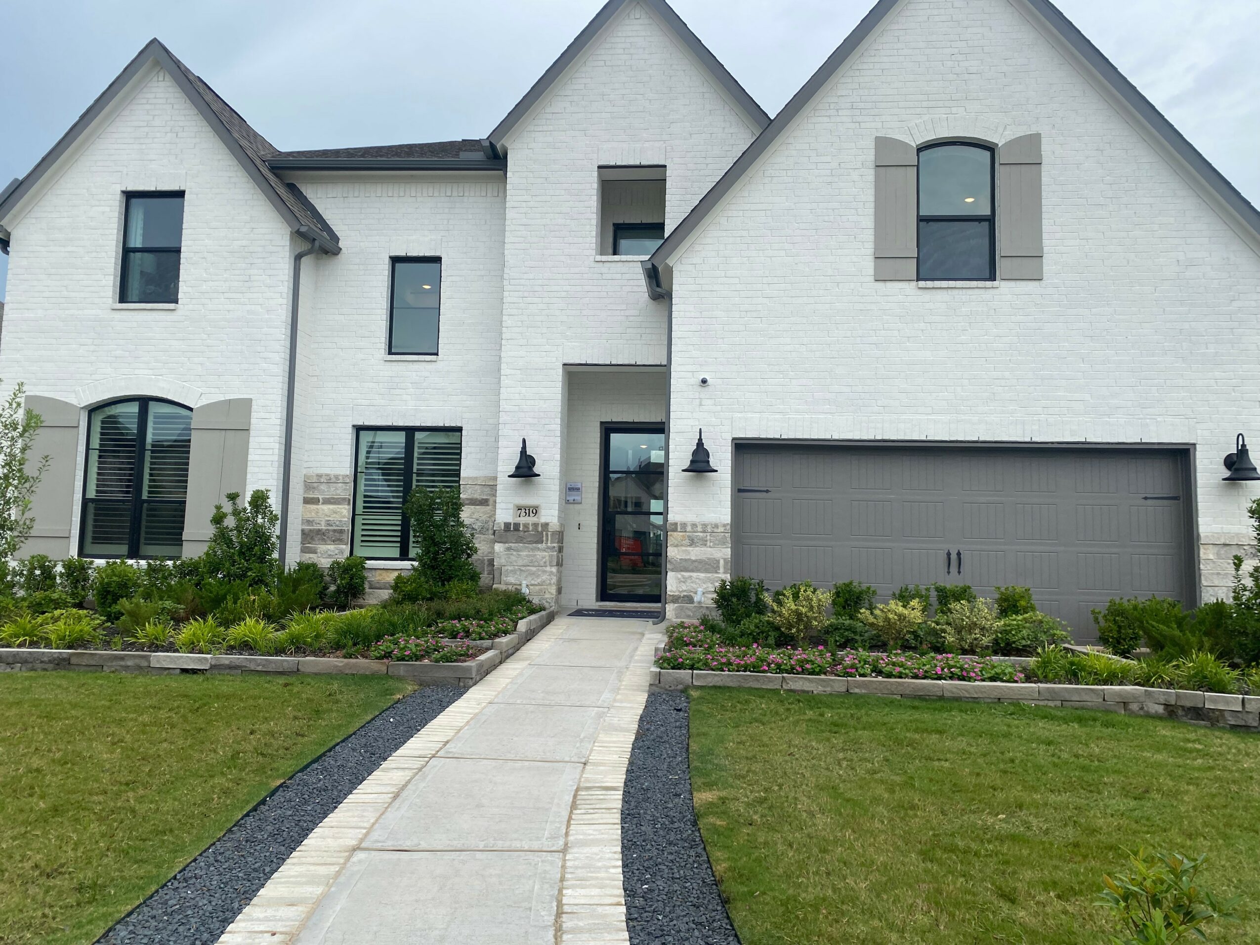 White modern house with a driveway, front garden, and multiple windows, under a cloudy sky.