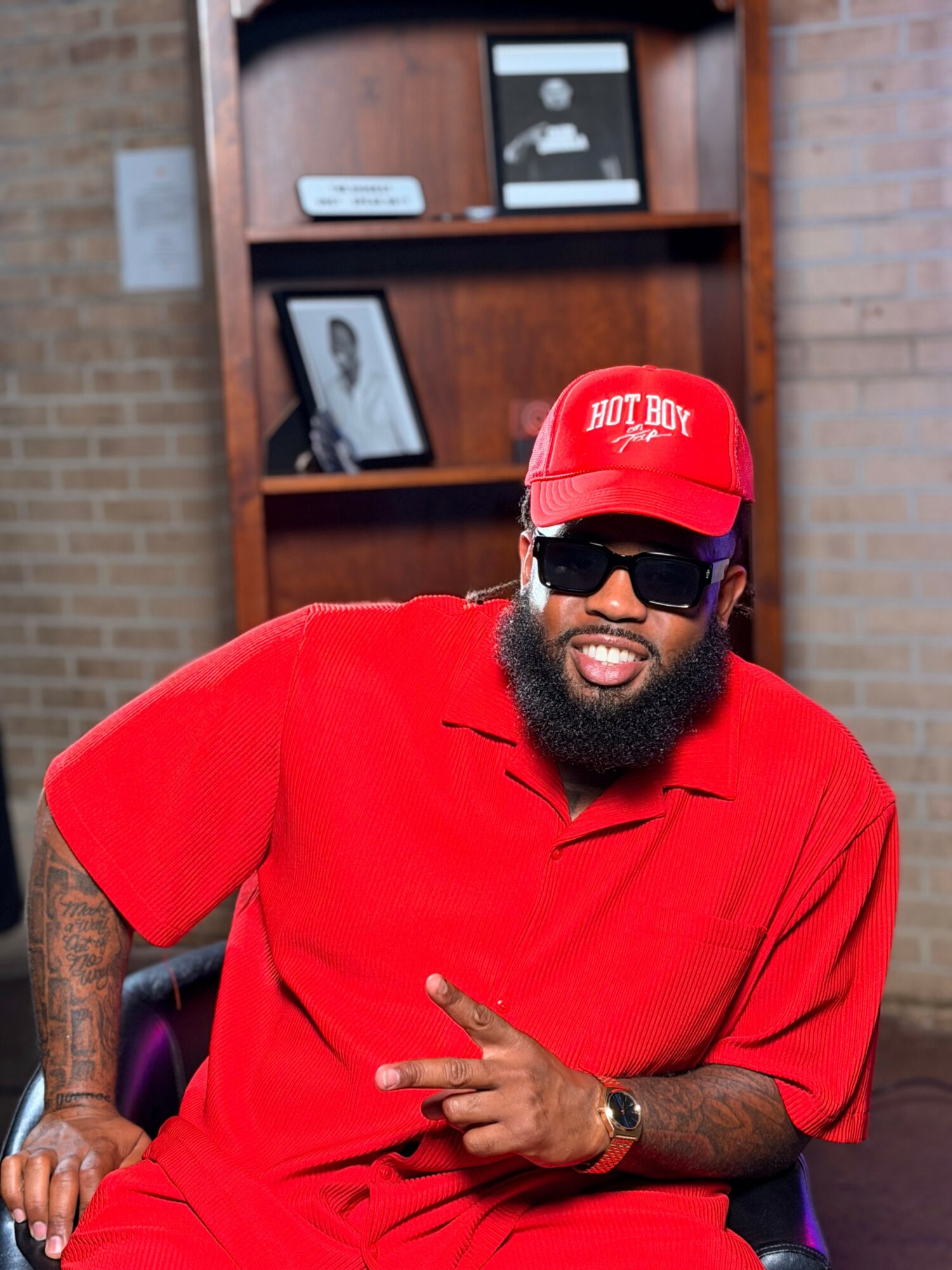 Man with a beard wearing sunglasses, a red cap, and a red shirt, making a peace sign gesture indoors.