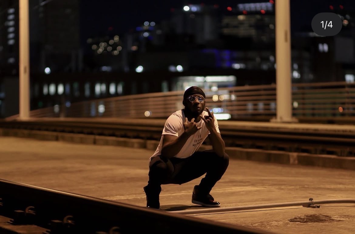 Person crouching on train tracks at night, city lights in background, holding a phone to their ear.