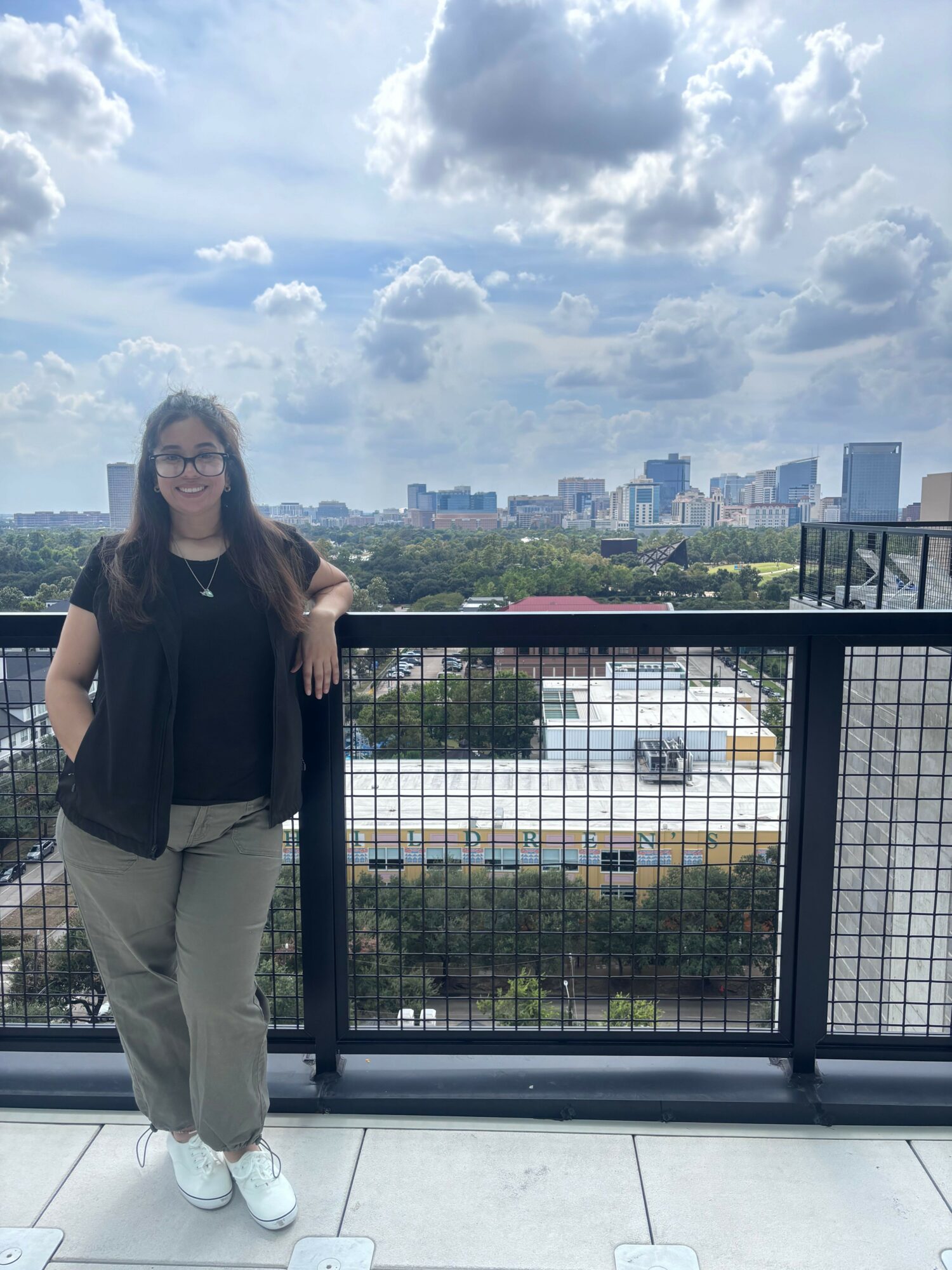 Person standing on balcony with city skyline and cloudy sky in background.