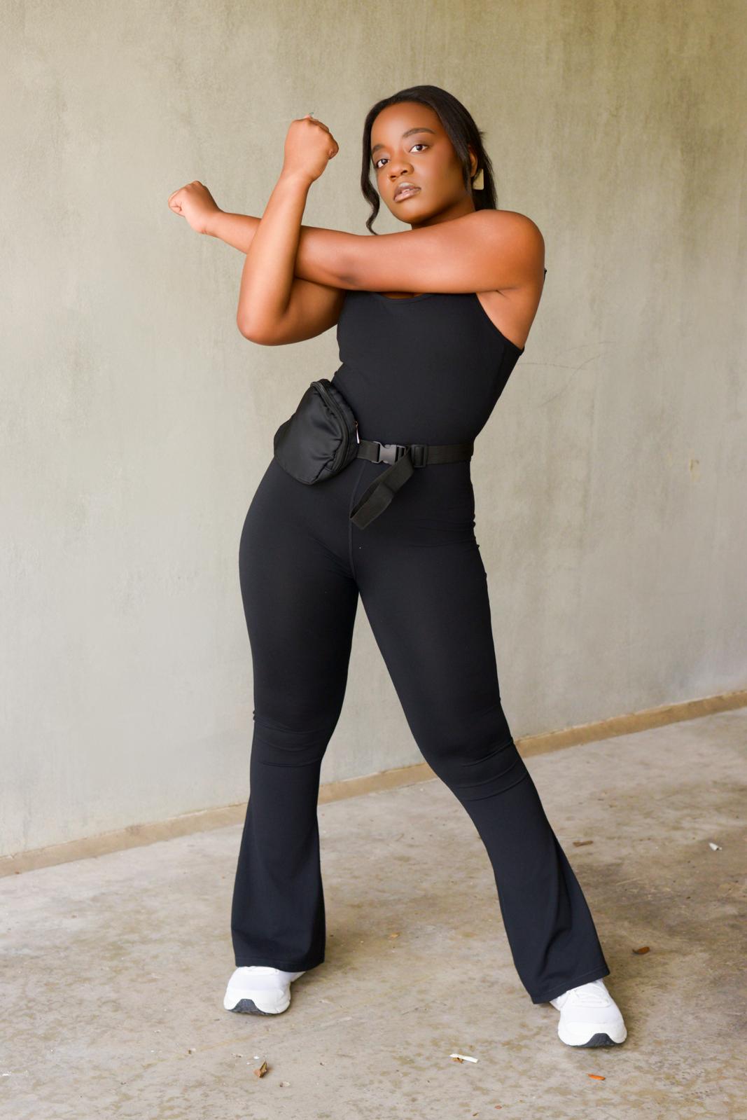 Woman in black outfit standing against a plain wall, arms crossed, looking at the camera.