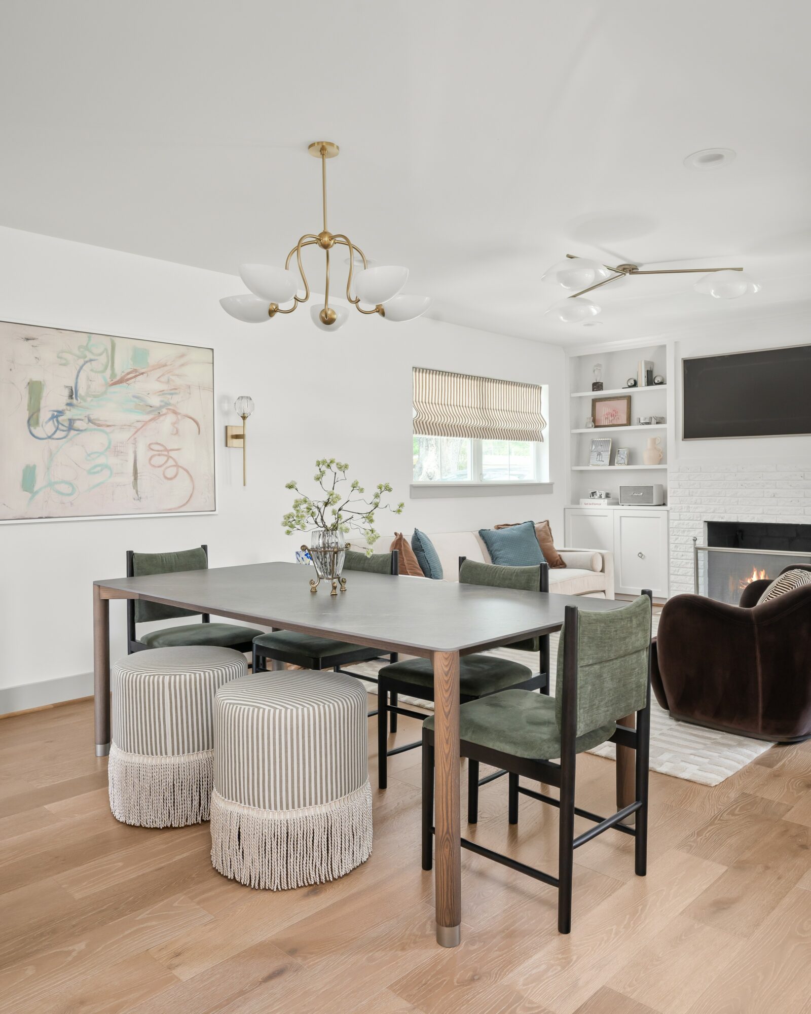 Living and dining room with a large table, chairs, a sofa, and a fireplace, decorated in neutral tones with wooden flooring.
