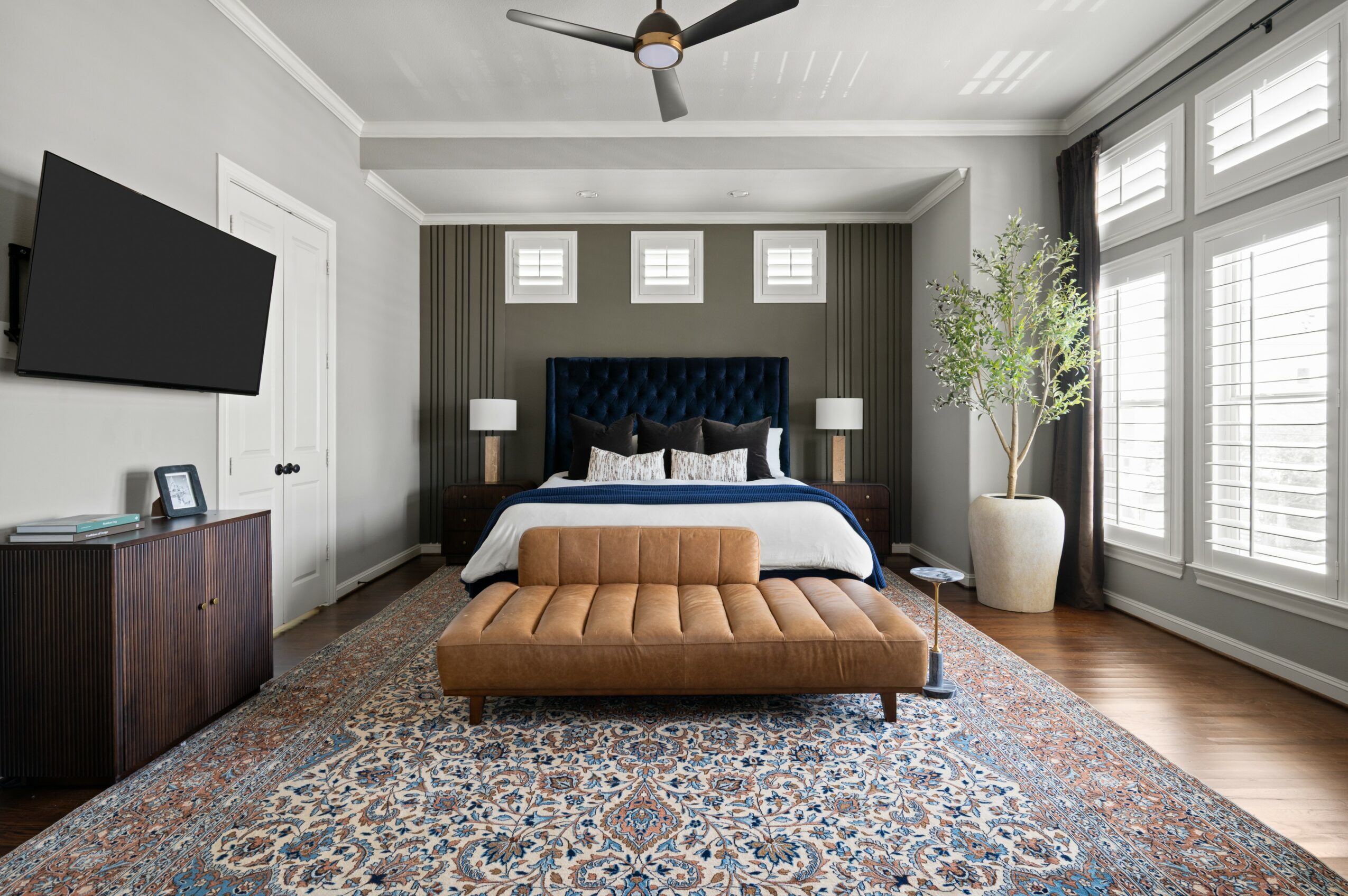 Bedroom with a bed, tufted headboard, large window, potted plant, TV, and a bench at the foot of the bed.