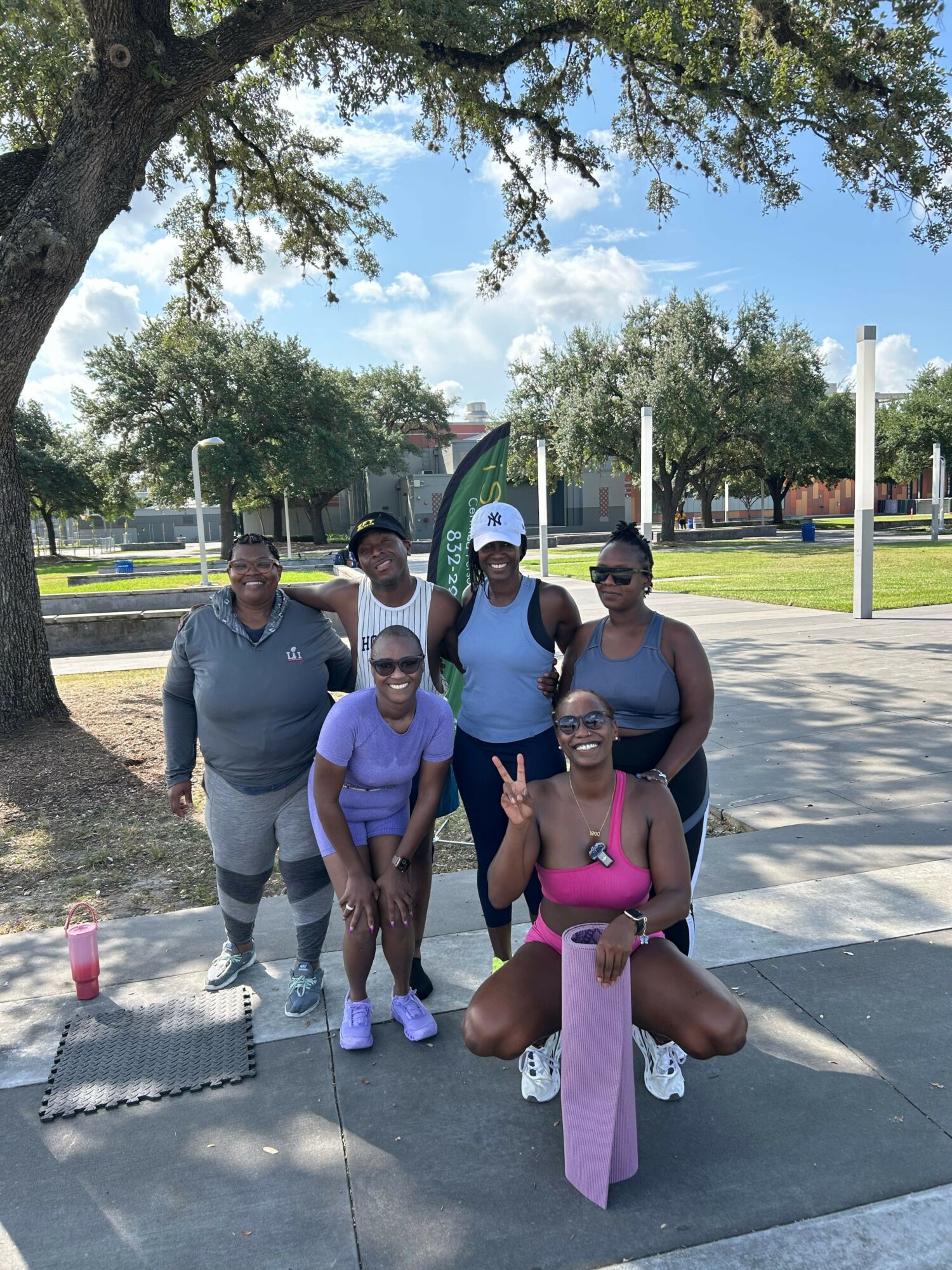 Group of five people standing outdoors on a sidewalk, with trees and a park in the background.