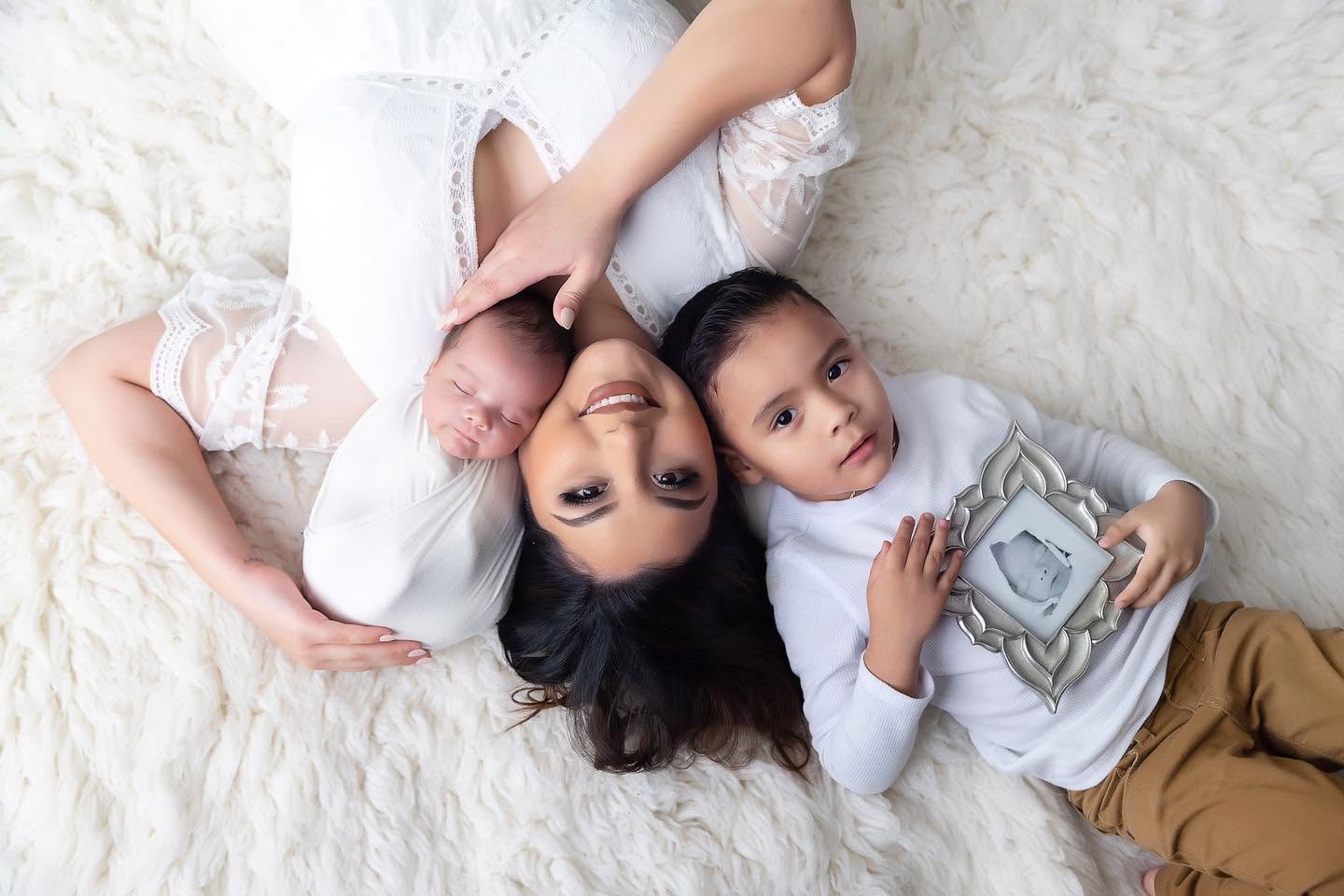 A woman and two children lying on a soft surface, smiling and holding a camera, viewed from above.