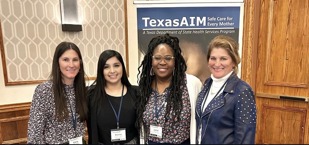 Four women standing together indoors, smiling, with a TexasAIM banner in the background.