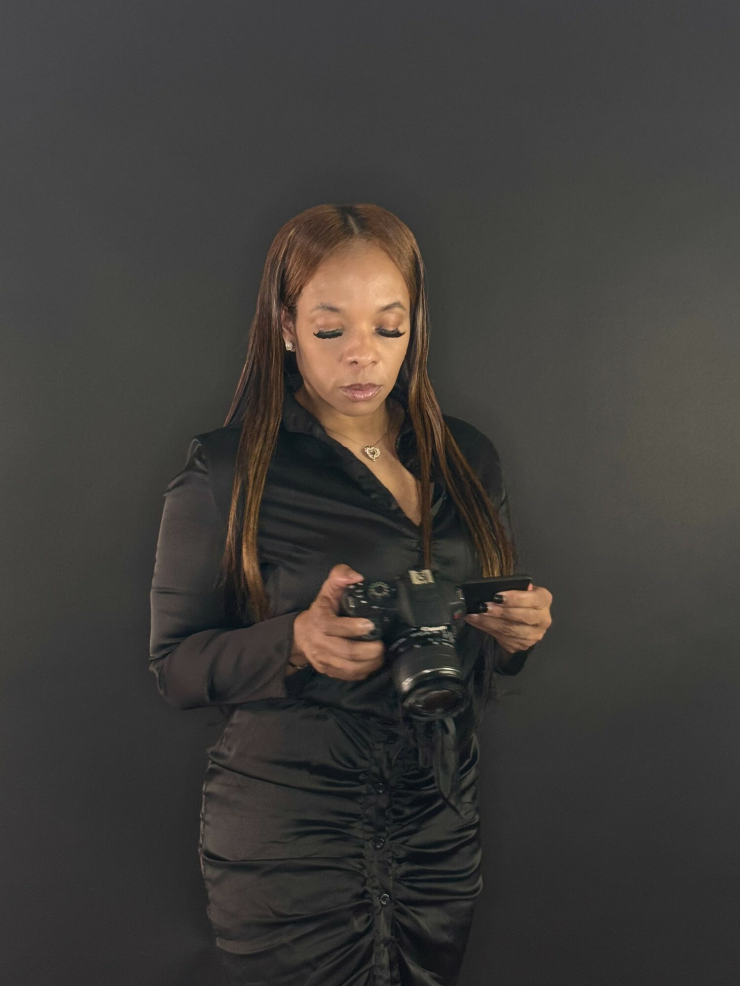 Woman with long hair holding a camera, standing against a dark background.